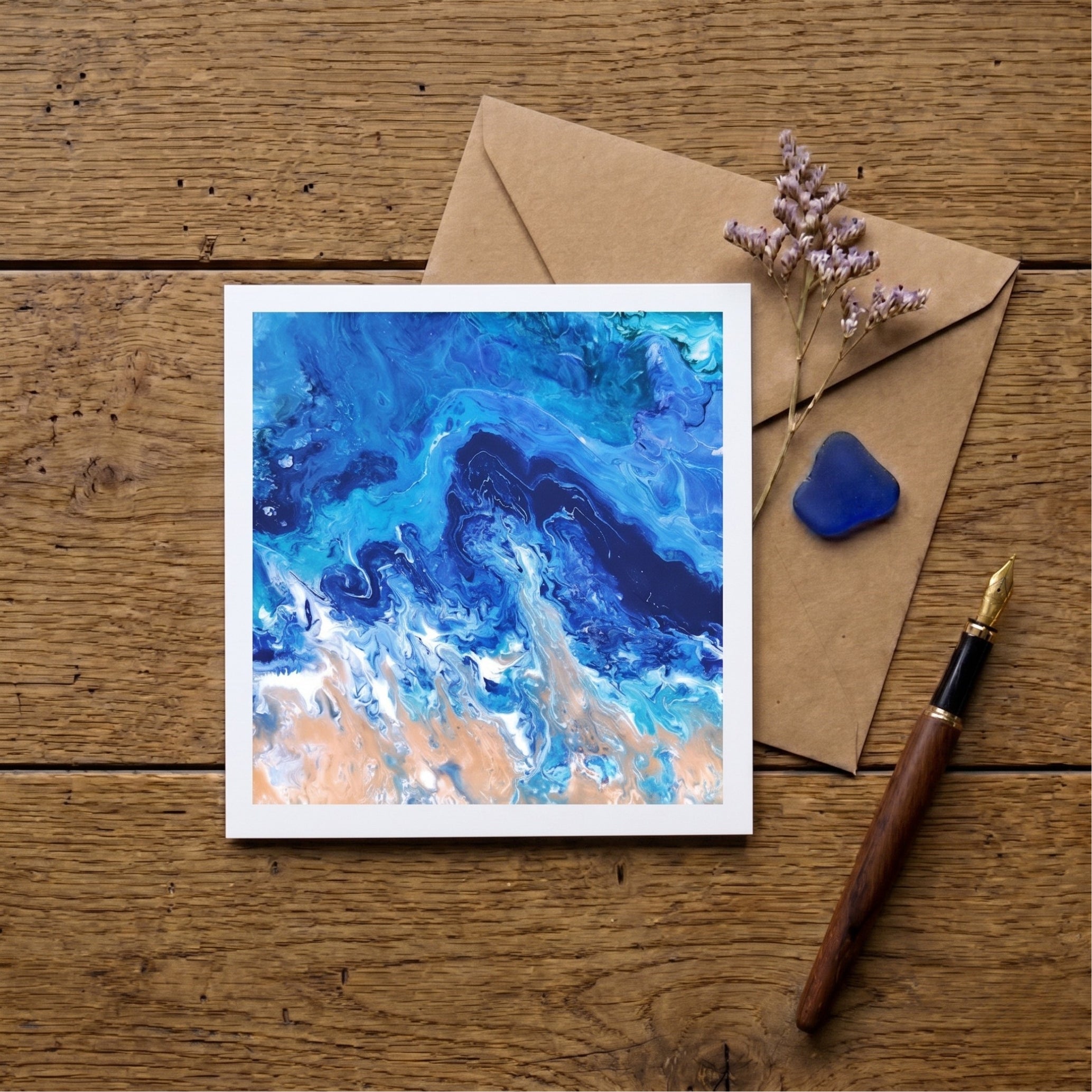 Artistic card with blue and white abstract design on a wooden surface with an envelope and pen.