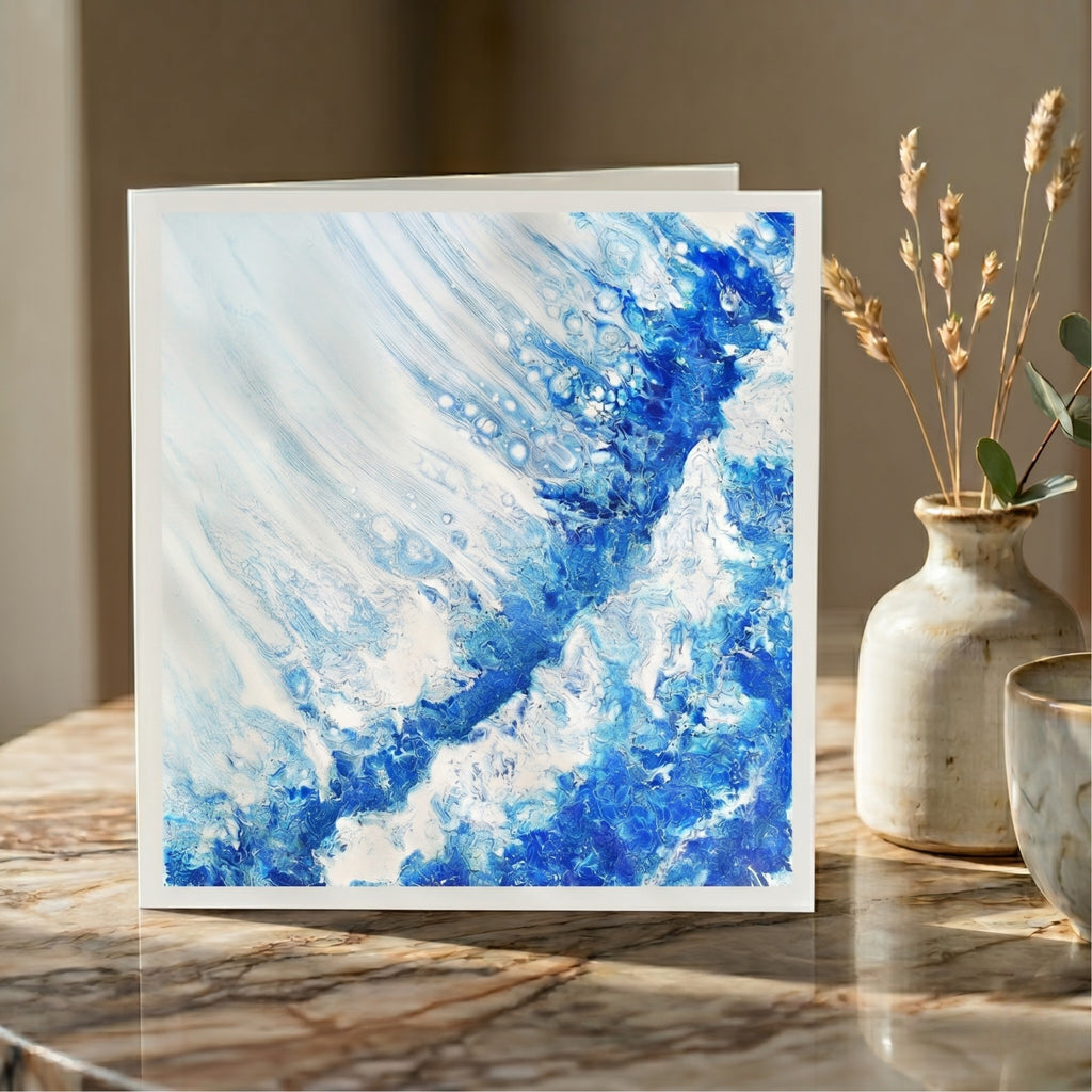 Abstract blue and white painting on a card displayed on a marble surface with decorative elements.