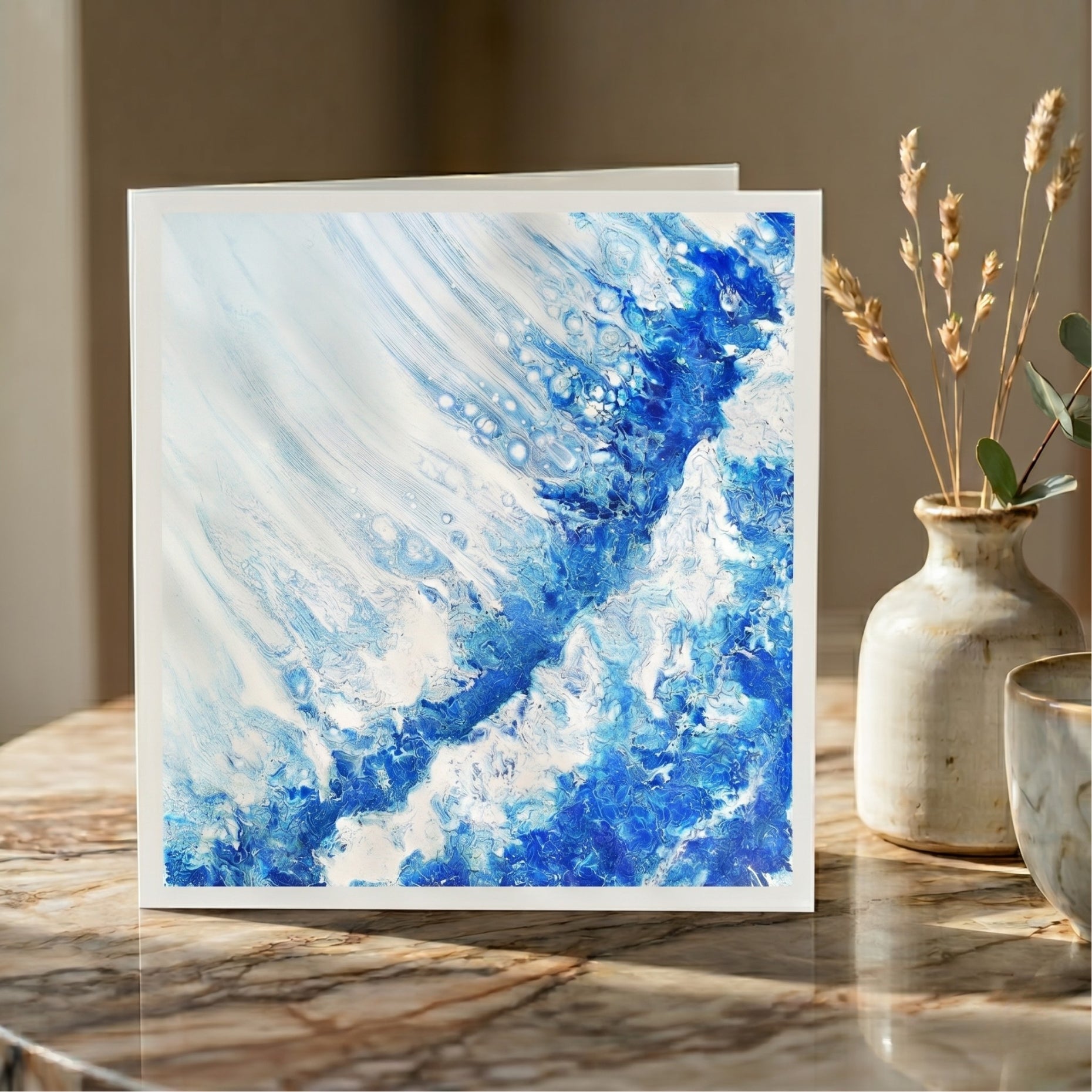 Abstract blue and white painting on a card displayed on a marble surface with decorative elements.