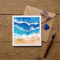 Card with beach design, envelope, pen, and decorative elements on wooden surface