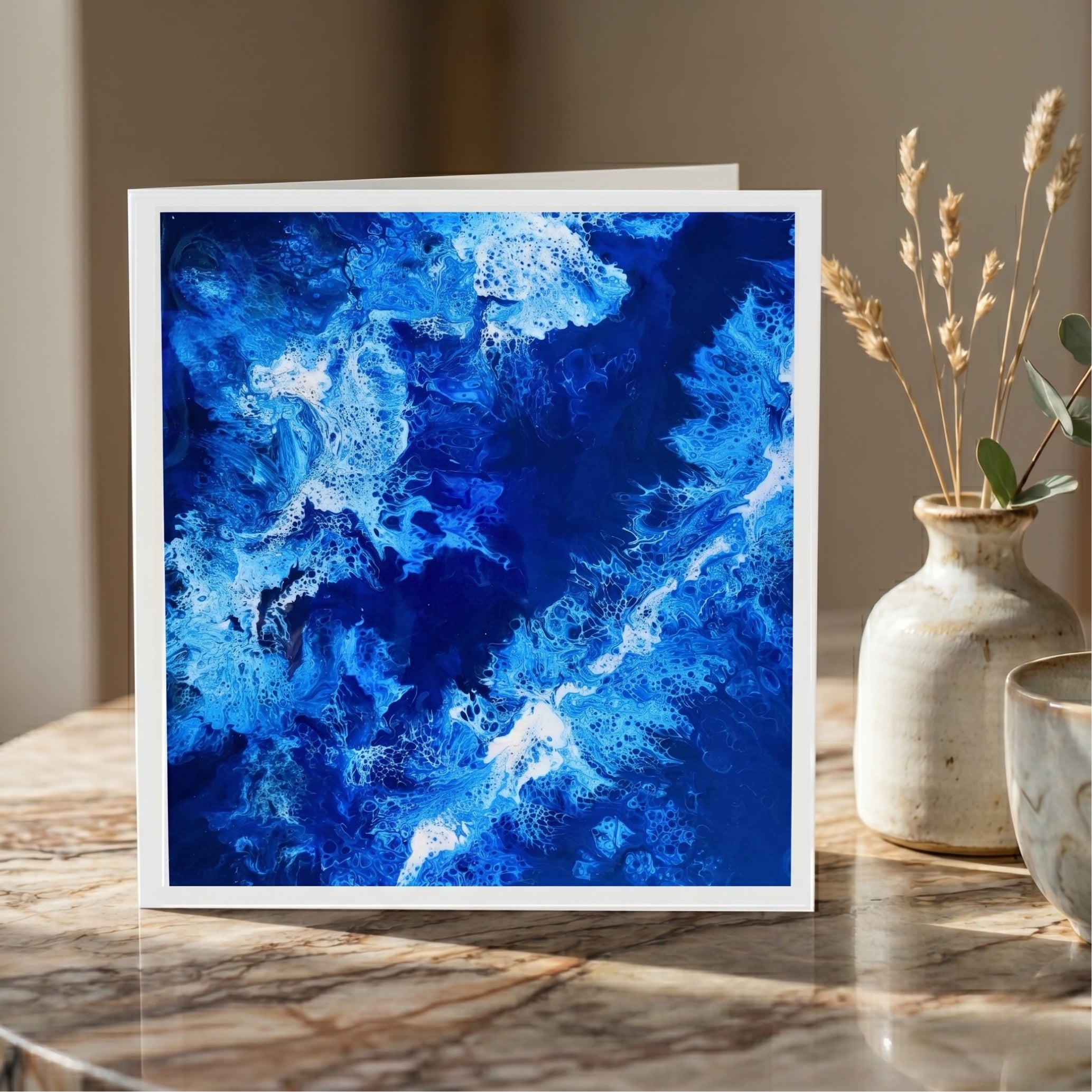 Framed abstract blue artwork on a marble surface with decorative elements.