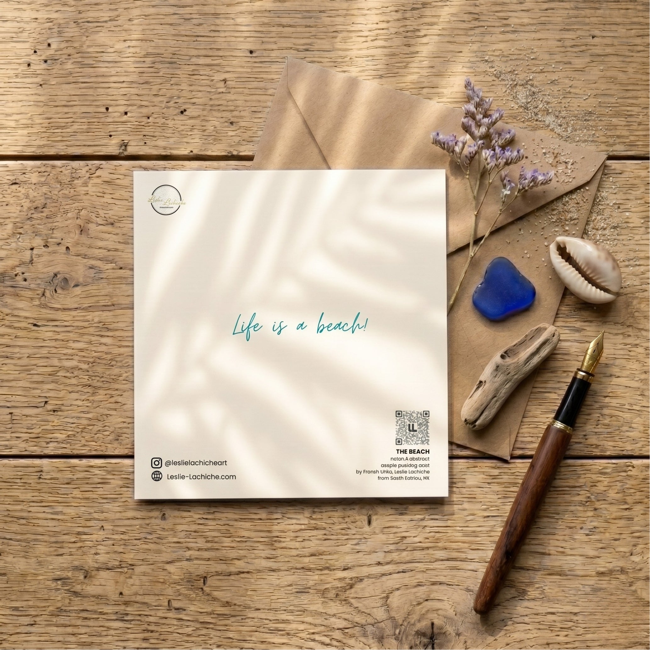 back  card with 'Life is a beach' text on a wooden surface with an envelope, flowers, and a pen.