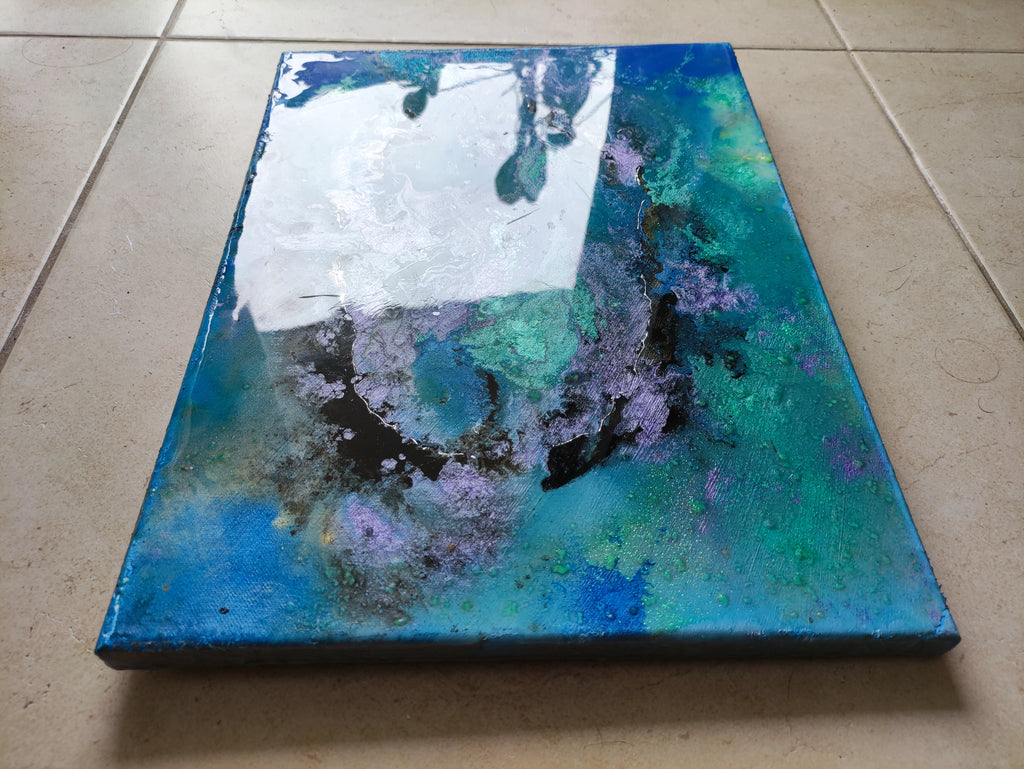 Abstract art piece on a canvas with blue, green, and purple colors on a tiled floor.