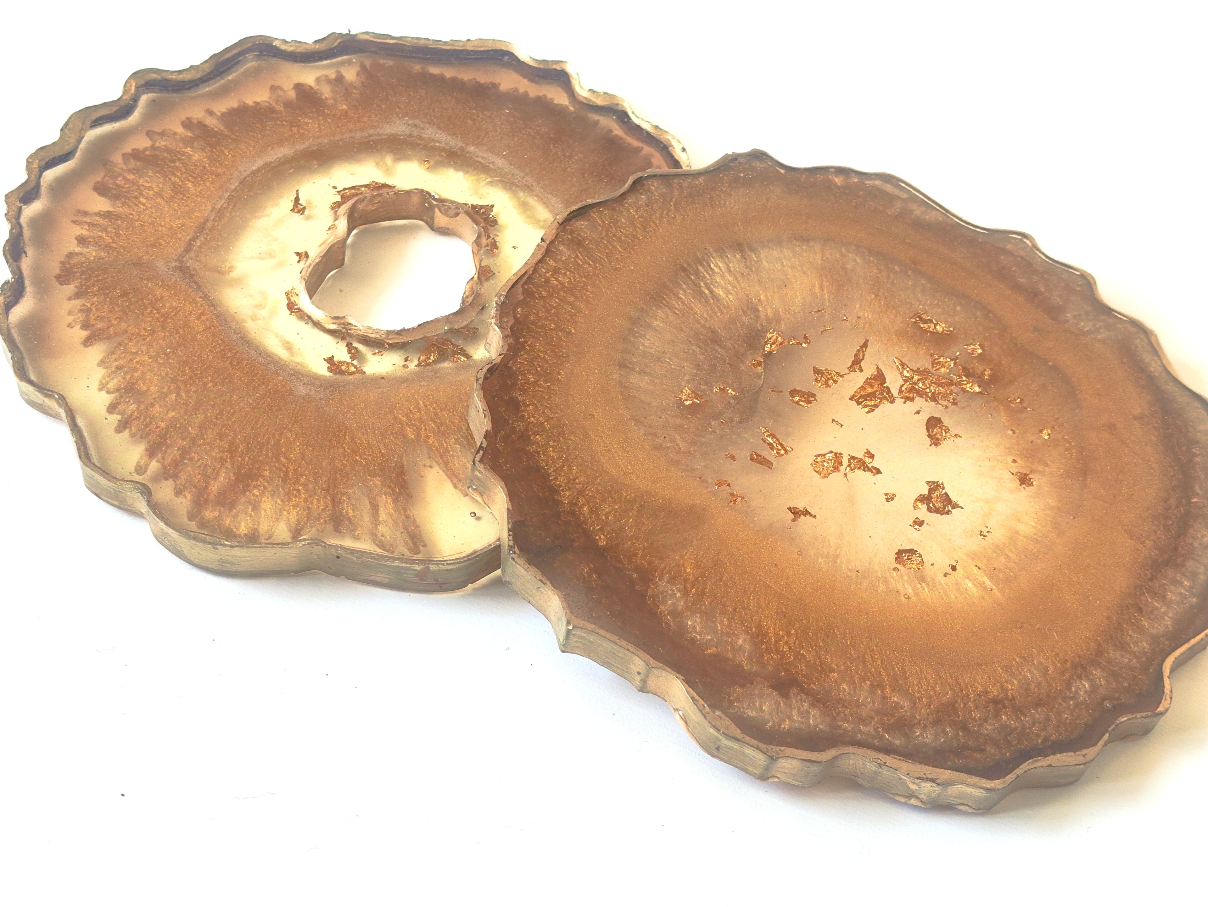 Two bronze-colored coasters with textured surfaces on a white background