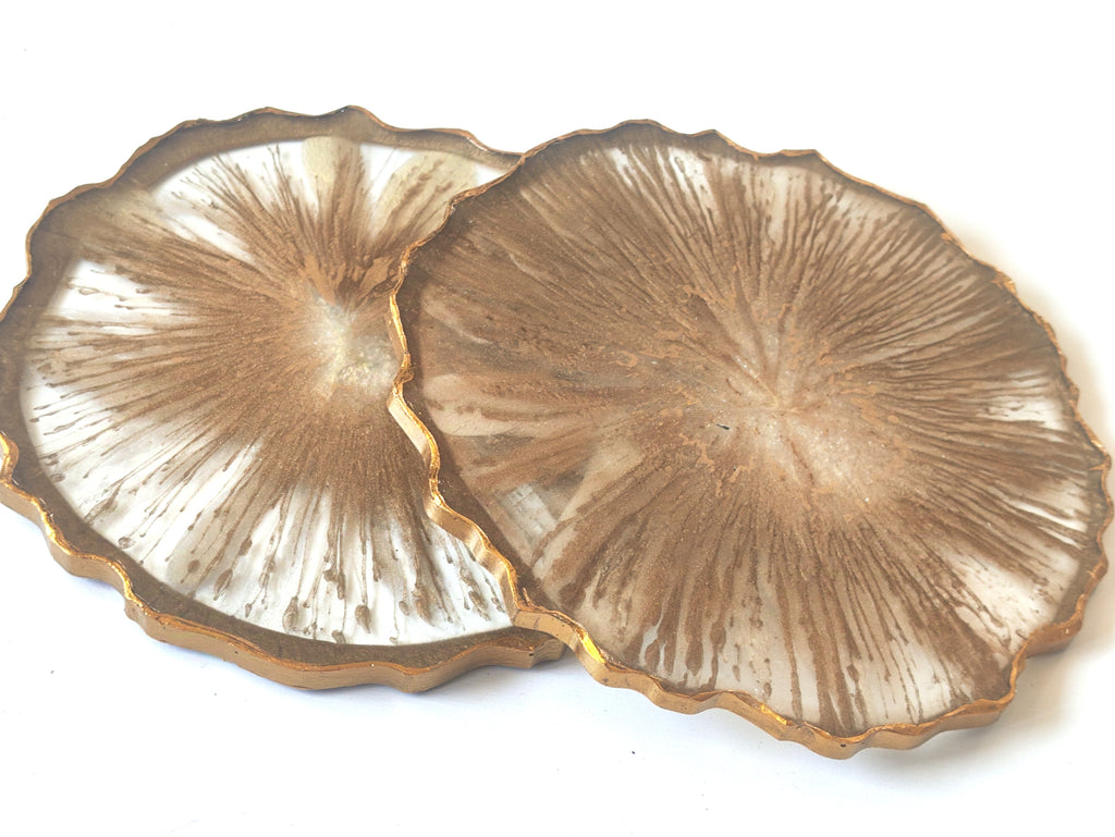 Two decorative coasters with a textured surface and gold edges on a white background