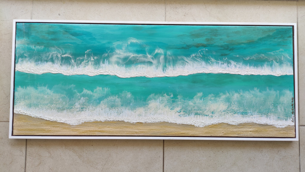 Framed artwork of a beach scene with turquoise water and white waves on a beige wall.