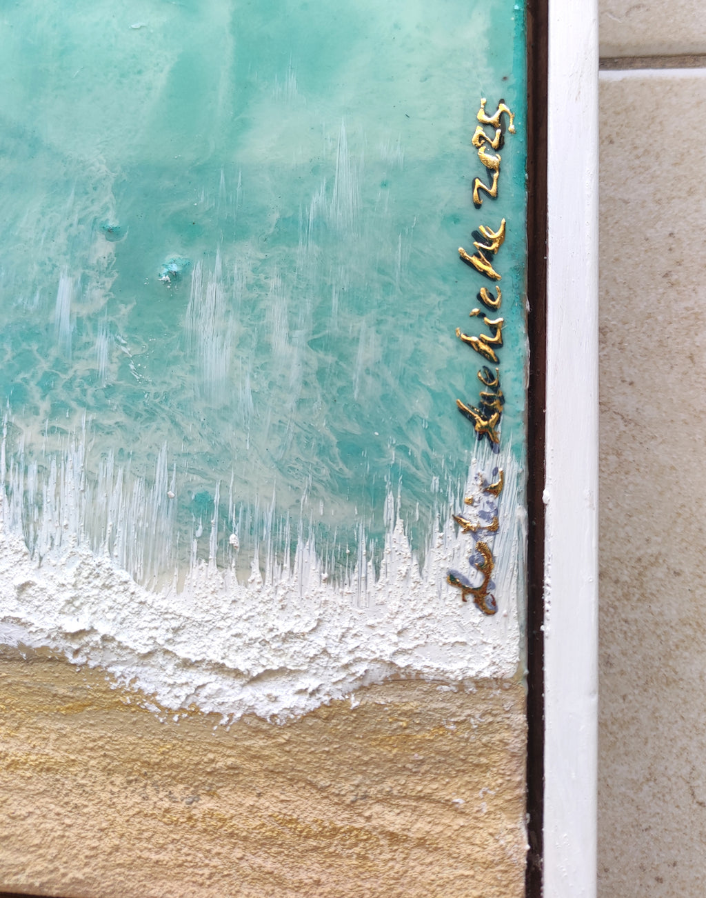 Artistic depiction of a beach scene with turquoise water and sand, featuring a brand name.