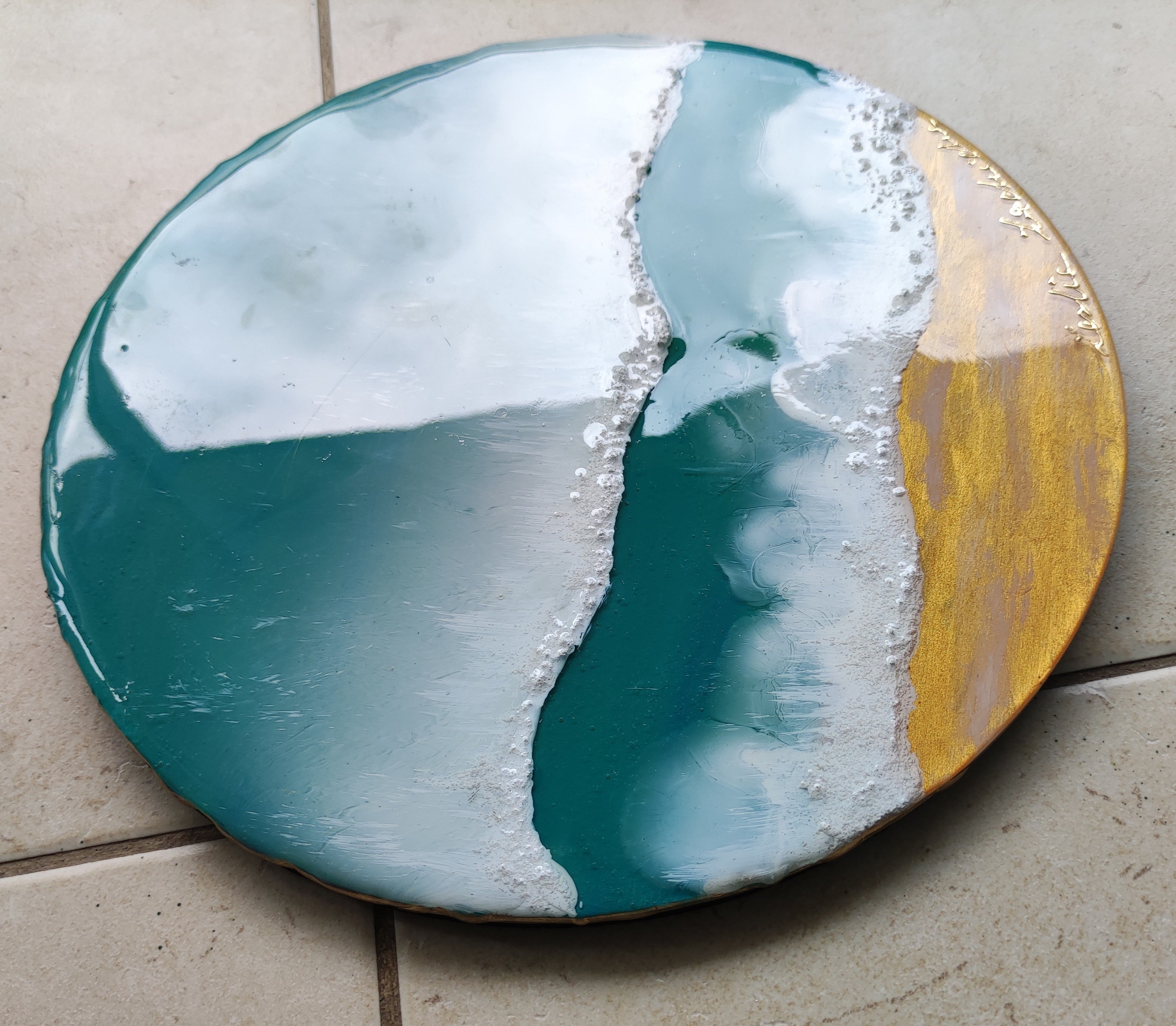 Round decorative plate with a gradient design of blue, white, and gold on a tiled floor.