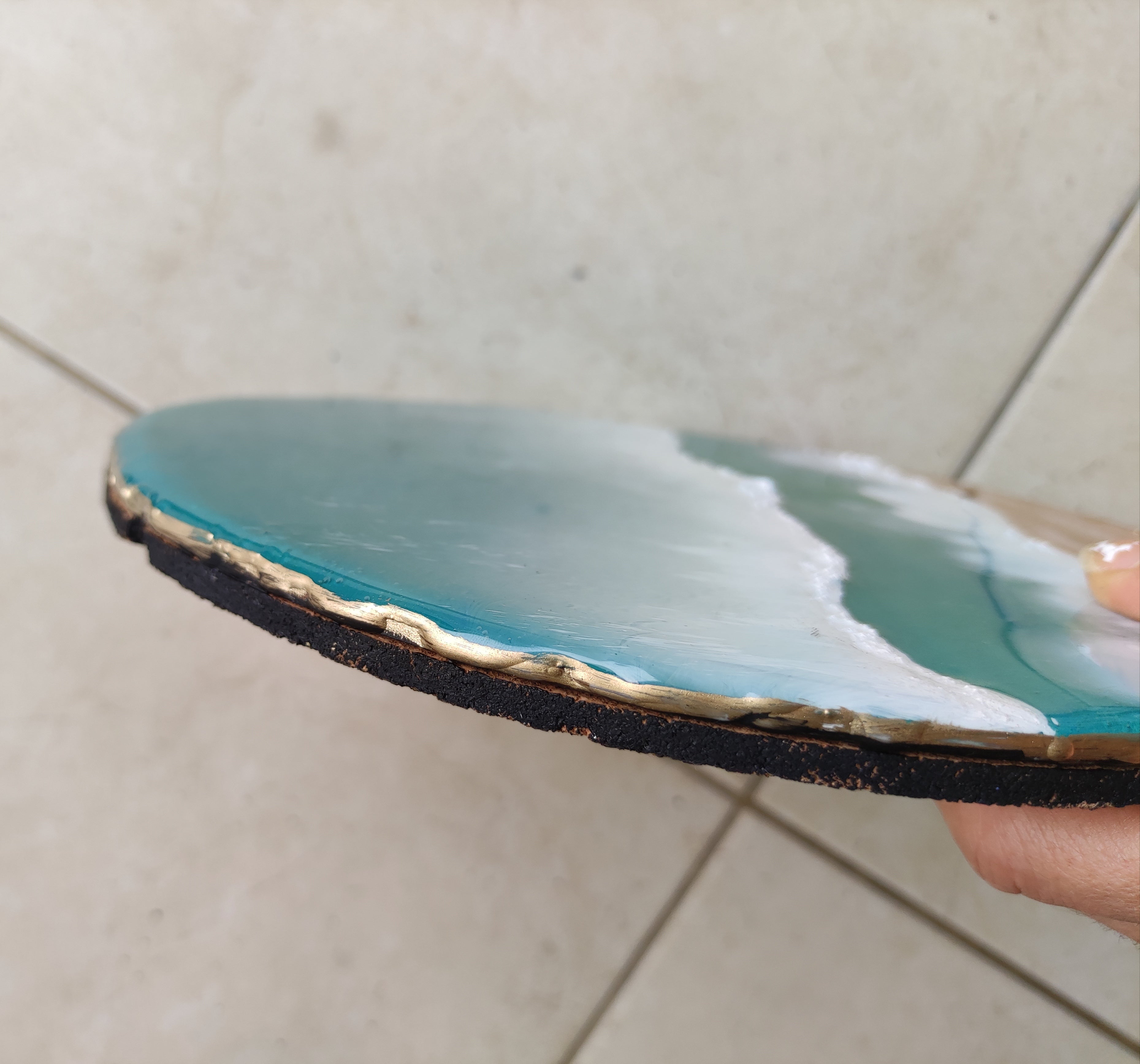 Close-up of a blue agate stone with gold rim held by a hand on a tiled floor.