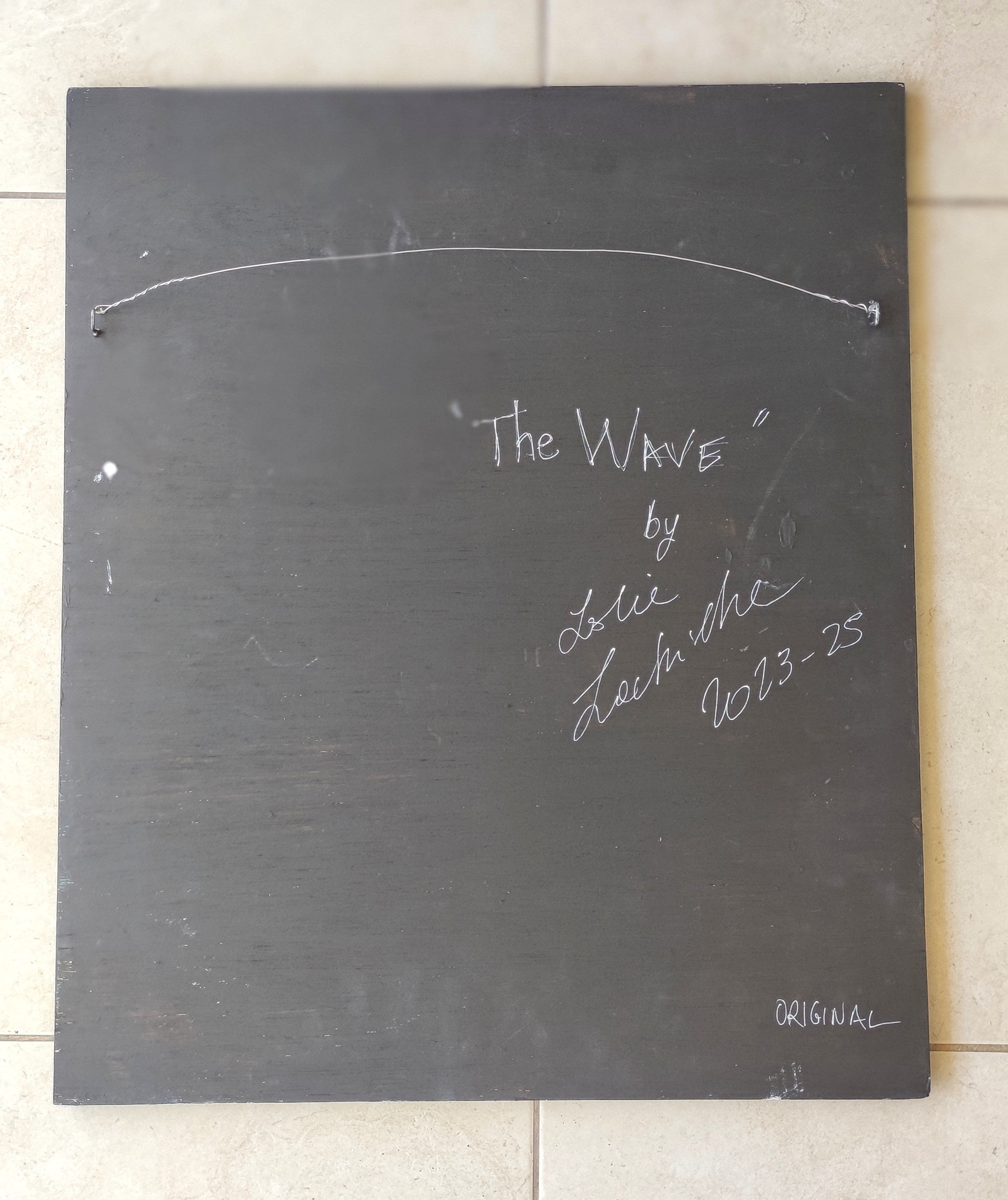 Blackboard with 'The Wave' by Lole Lole signature and date on a tiled floor.
