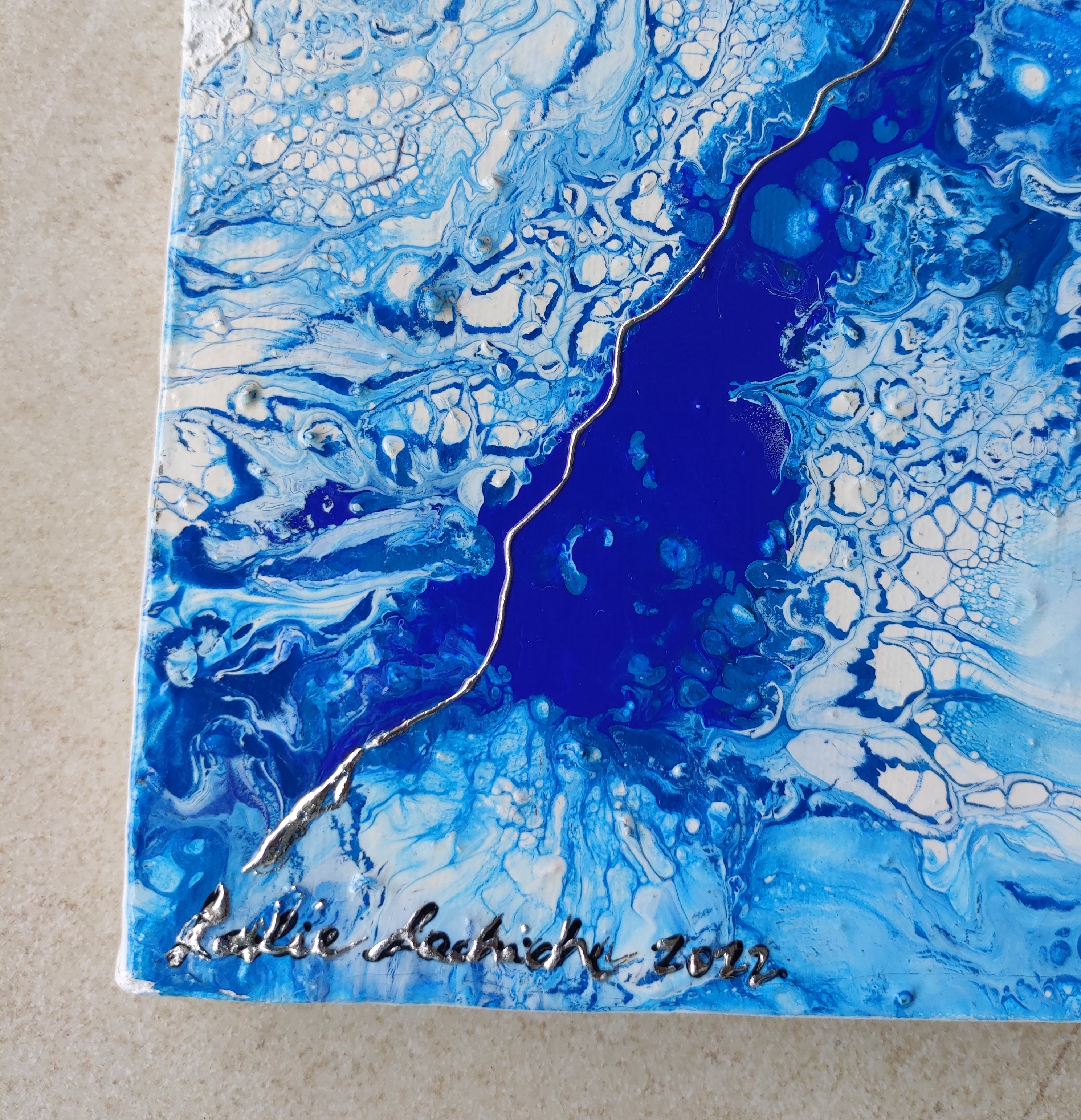 Artistic blue and white abstract design on a textured surface, signed 'Julie Lachic' with the year 2022.