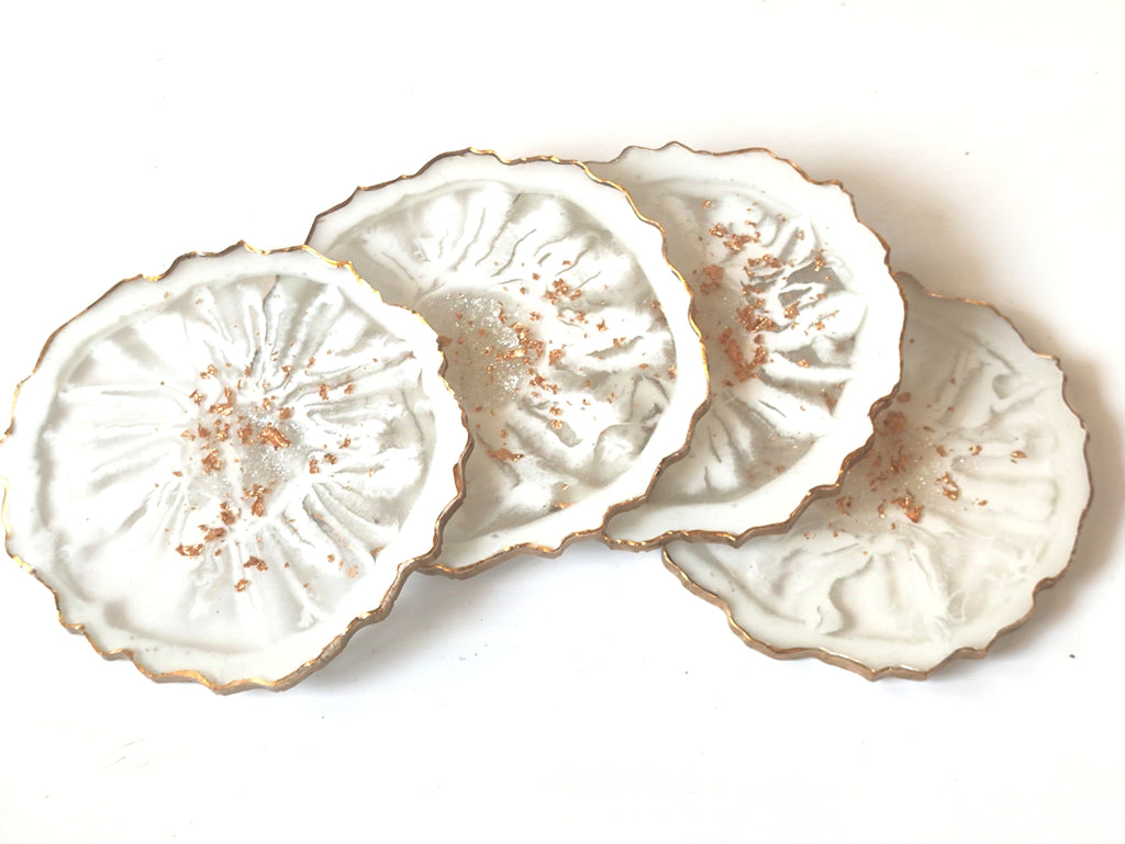 Set of four white ceramic coasters with decorative edges on a white background